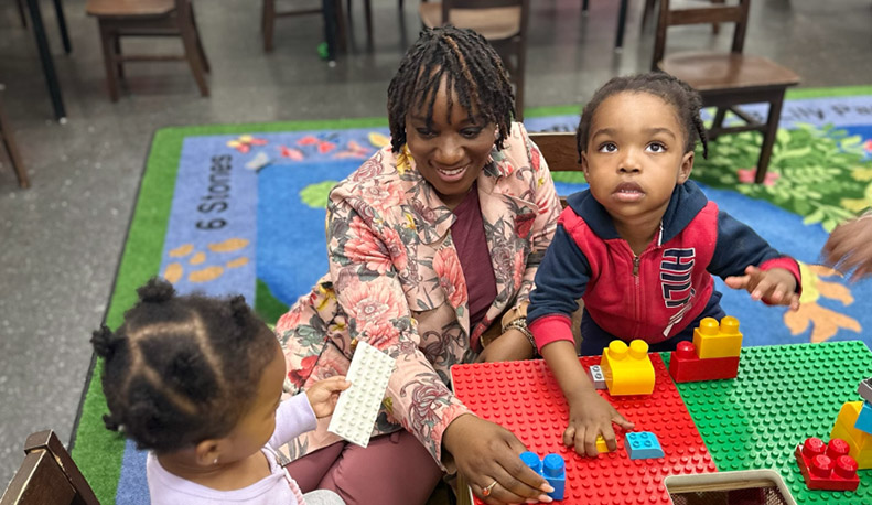 Child care educator smiling and playing with legos with 2 children